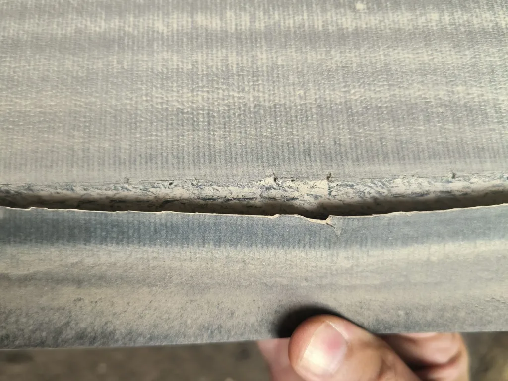 A visible separation has developed between carcass layers, a damage pattern that should prompt checks of bending, adhesion, impact and local stress conditions.